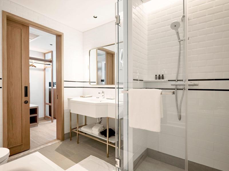 Moderner Badbereich mit Glasdusche, weißem Waschbecken und Holz-Akzenten am Türrahmen.