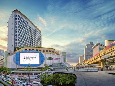 Modernes Stadthotel mit hohem Gebäude, großer Werbetafel und belebter Straße bei Sonnenuntergang