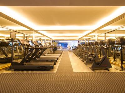 Großer Fitnessraum mit zahlreichen Laufbändern und anderen Trainingsgeräten in warm beleuchtetem Raum.