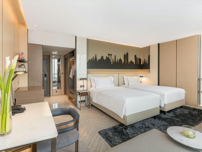 Modernes Hotelzimmer mit zwei Einzelbetten, Schreibtisch und großer Fensterfront mit Stadtblick.