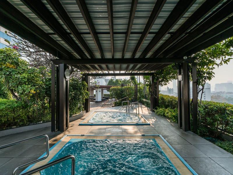 Whirlpool unter einem überdachten Bereich mit Blick auf eine ruhige Gartenlandschaft.