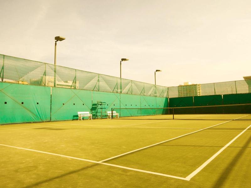 Leerer Tennisplatz mit grünen Wänden und Spielbänken bei bewölktem Himmel.