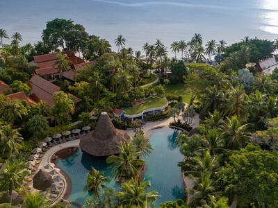 Blick auf ein tropisches Resort mit Pool, Palmen und Meer im Hintergrund.