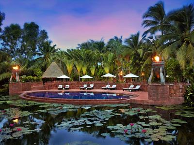 Pool mit Liegestühlen und Sonnenschirmen umgeben von üppiger tropischer Vegetation bei Dämmerung.