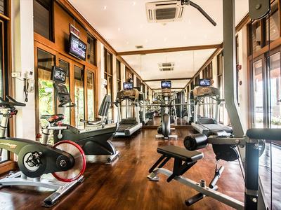 Heller Fitnessraum mit Holzfußboden und modernen Trainingsgeräten neben großen Fenstern.