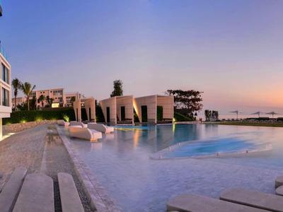 Moderne zwembadruimte met ligstoelen, bomen en hotelgebouw bij zonsondergang.