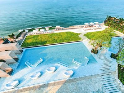 Moderner Infinity-Pool mit Liegen am Meer und Blick auf tropische Pflanzen.