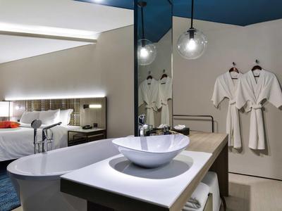 Modern hotelkamer met vrijstaand bad, wastafel en badjassen aan de muur.