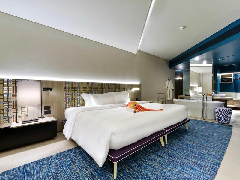 Modernes Hotelzimmer mit geneigter Decke, großem Bett, blauem Teppich und stilvollem Badezimmer.