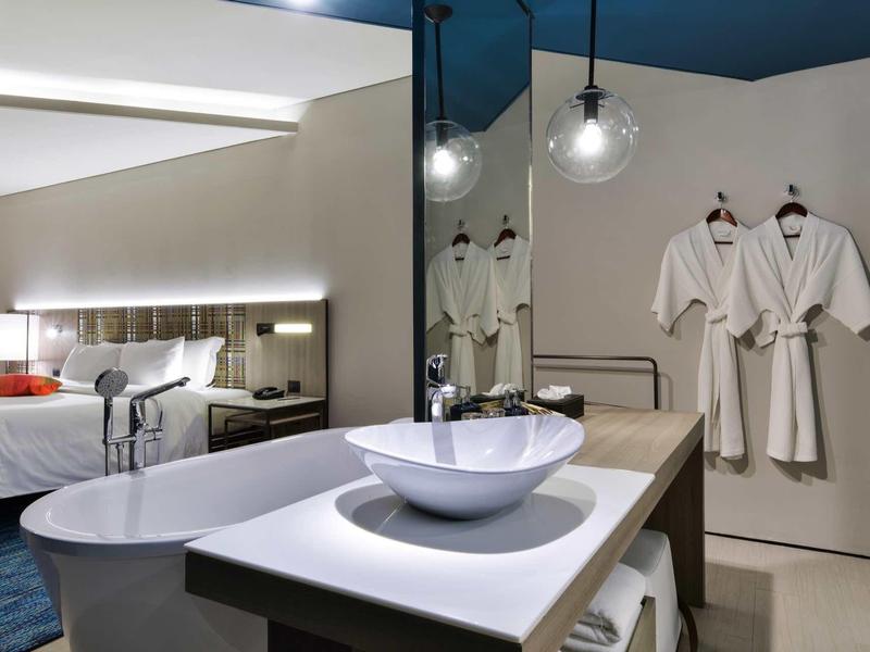 Modernes Hotelzimmer mit offenem Bad und Doppelbett in neutren Farben