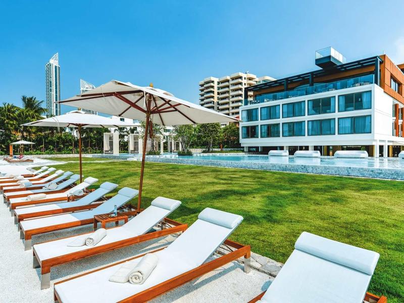 Moderne Hotelanlage mit Liegestühlen und Sonnenschirmen auf einer gepflegten Wiese bei klarem Himmel.