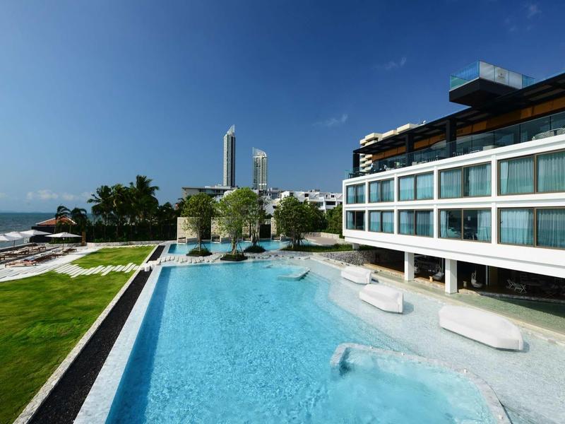 Modernes Hotel mit großem Pool, angrenzendem Rasen und Meerblick bei sonnigem Wetter.