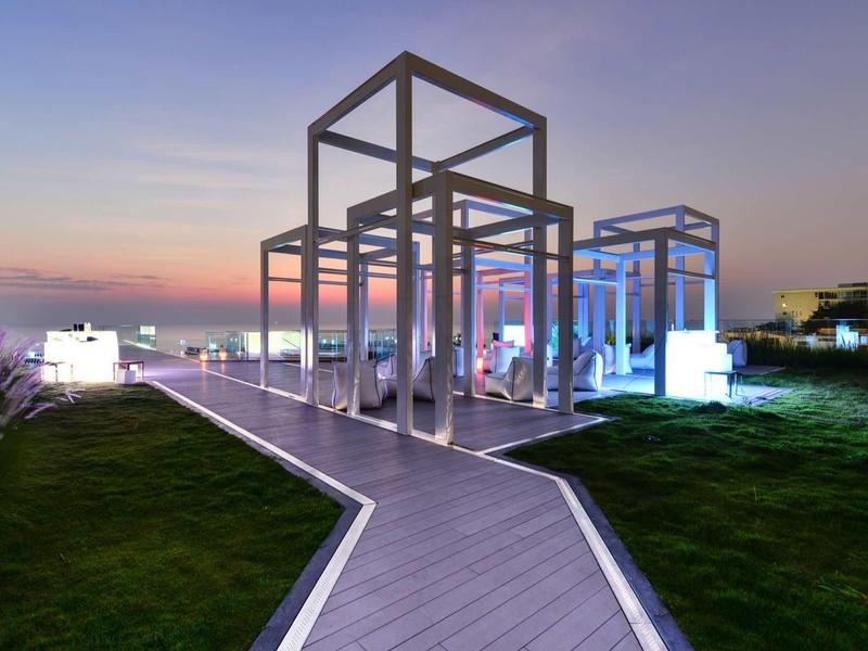 Moderner Pavillon aus Metallrahmen mit beleuchteten Sitzbereichen bei Sonnenuntergang.