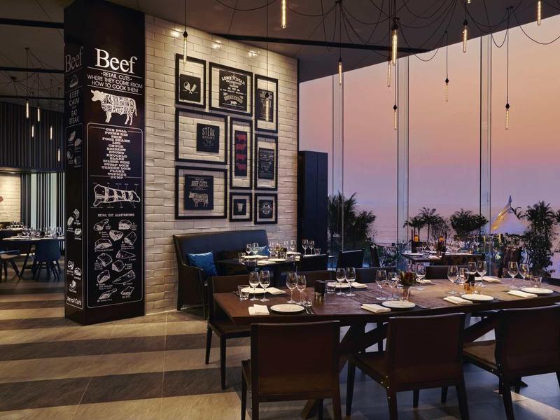 Elegantes Restaurant mit Holzböden, großem Fenster, modernem Mobiliar und Sonnenuntergangshimmel.