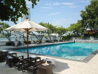 Poolbereich mit Liegestühlen, Sonnenschirm und Blick auf Wasser und Bäume bei klarem Himmel.