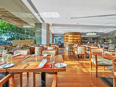 Moderner, heller Restaurantbereich mit Holztischen, Stühlen und großen Glasfenstern, viele gedeckte Plätze.