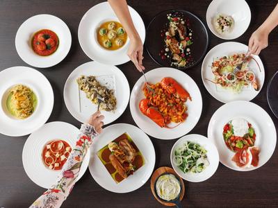 Verschiedene bunte Gerichte auf weißen Tellern auf einem dunklen Tisch, Hände reichen danach.