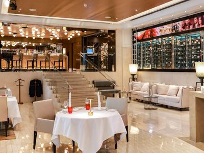 Eleganter Hotel-Loungebereich mit Bar, Treppe und Sitzbereichen, warmes Licht und moderne Einrichtung.