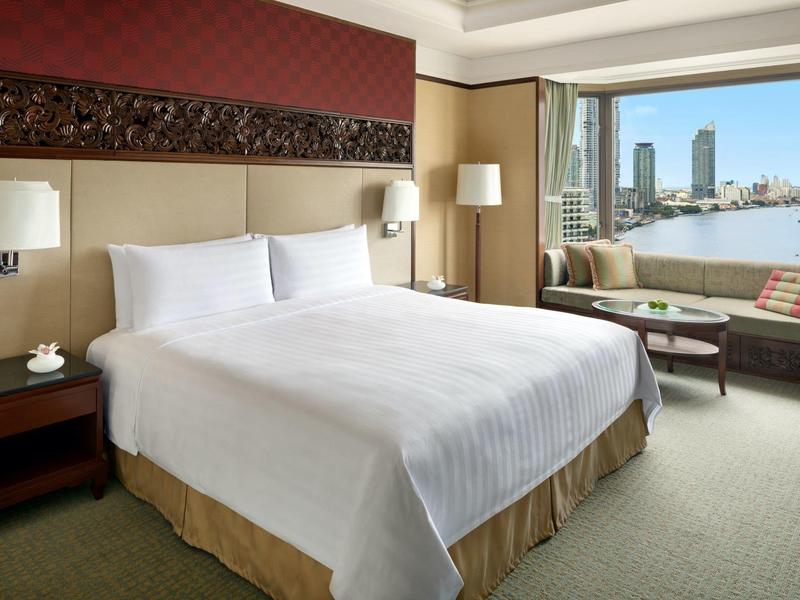 Hell eingerichtetes Schlafzimmer mit großem Bett, Nachttischen, Fenster mit Flussblick und Sofa.