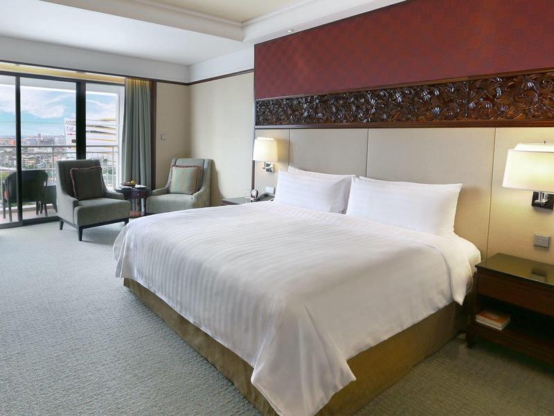 Modern eingerichtetes Schlafzimmer mit großem Bett, zwei Sesseln, Nachttisch und Fenster mit Vorhängen.