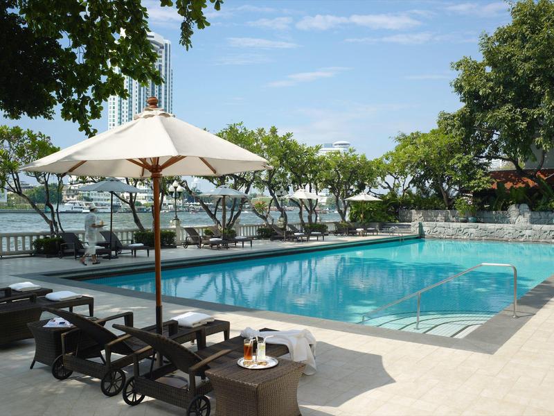 Ein klarer Pool mit Sonnenschirmen, Liegestühlen und grünen Bäumen im Hintergrund bei Tageslicht.