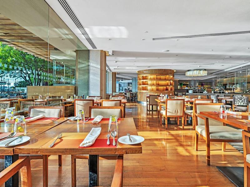 Moderner, heller Restaurantbereich mit Holztischen, Stühlen und großen Glasfenstern, viele gedeckte Plätze.