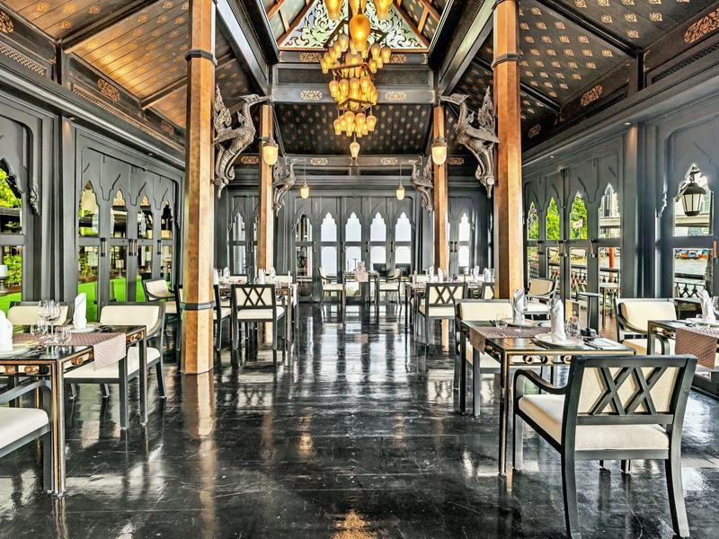 Großer, eleganter Speisesaal mit hohen Decken, dunklem Boden, goldenen Lampen und modernen Stühlen.