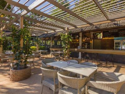 Offener Außenbereich mit Tischen, Stühlen und viel grüner Pflanzen unter Holzpergola.