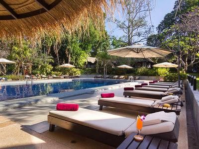 Poolbereich mit Liegen, Sonnenschirmen und tropischer Bepflanzung an einem sonnigen Tag.