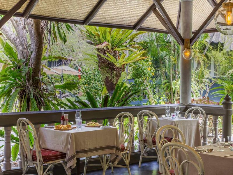 Gemütlicher Außenbereich eines Restaurants mit gedeckten Tischen und grünem Dschungel im Hintergrund.