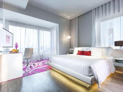 Modernes Hotelzimmer mit großem Bett, Schreibtisch und großen Fenstern mit weißen Vorhängen.