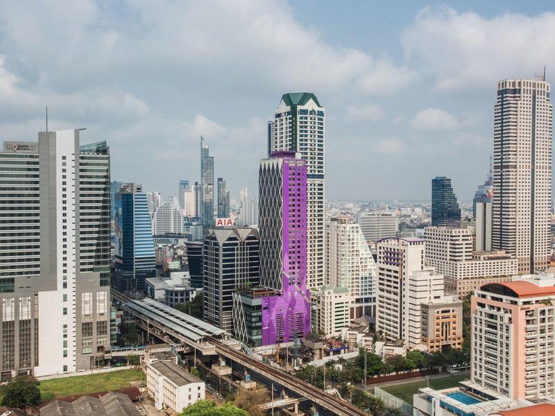 Städtische Skyline mit Wolkenkratzern, darunter ein violettes Hochhaus und eine Hochbahnlinie.