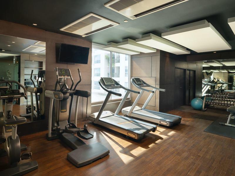 Moderner Fitnessraum mit Laufbändern, Crosstrainern und Spiegelwand, Holzboden und natürlichem Licht.