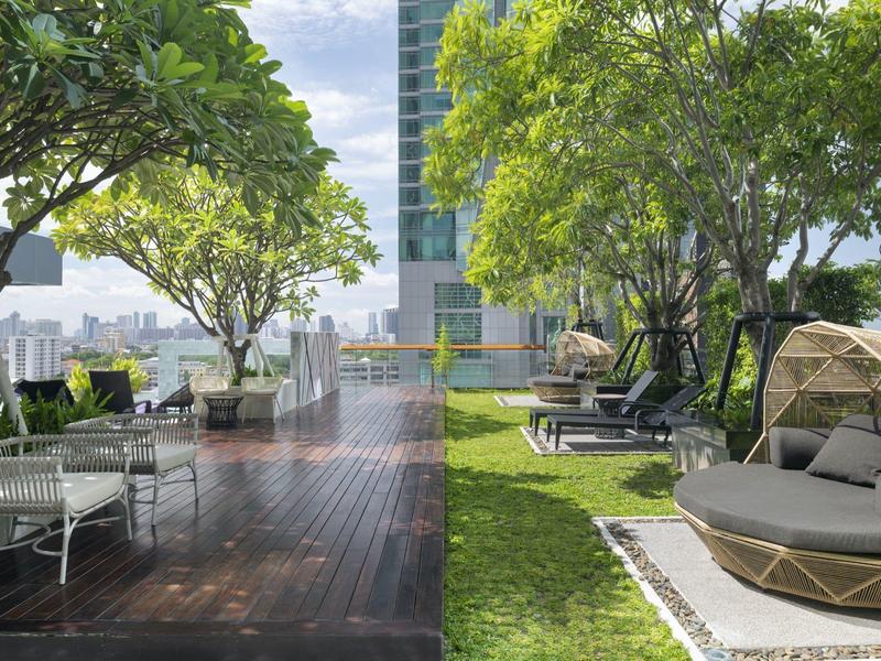 Moderner Außenbereich mit Holzboden, Liegen und Grünflächen unter großen Bäumen bei Tageslicht.