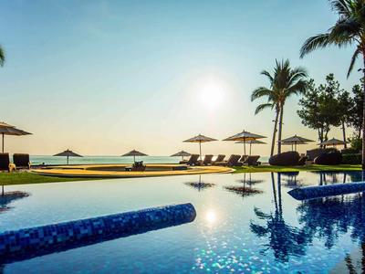 Pool mit Sonnenschirmen und Palmen bei Sonnenuntergang am Meer