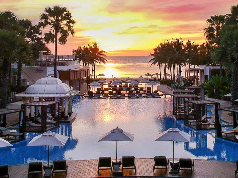 Luxurious pool area with palm trees and sunset over the sea at the hotel.