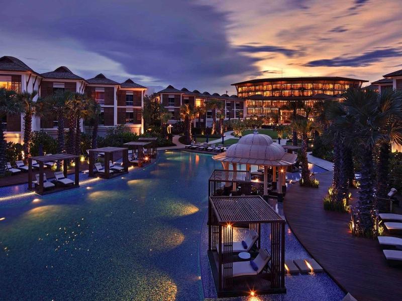 Evening view of a luxury hotel with illuminated pool and outdoor seating areas.