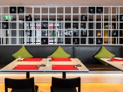 Modernes Restaurant mit grauem Polstersofa, grünen Kissen, roten Tischsets und schwarzem Stuhl.