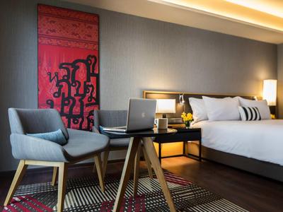 Moderně zařízený hotelový pokoj s pohodlným křeslem, psacím stolem a velkou postelí.