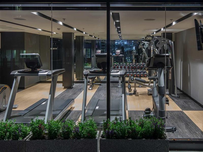 Moderner Fitnessraum mit Laufbändern, Hanteln, Spiegeln und Pflanzen vor großen Glasfenstern.