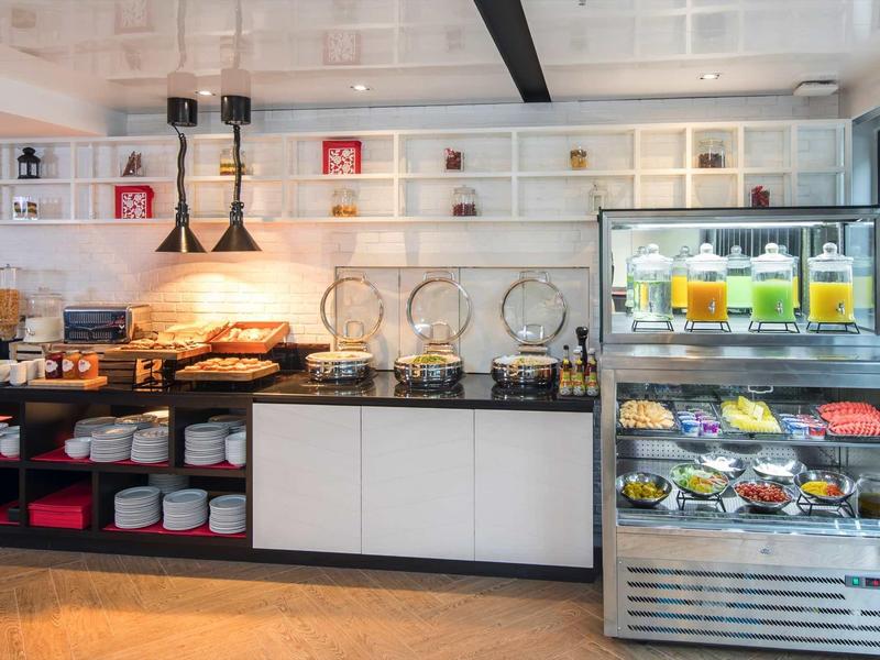 Buffet mit Getränkedispendern, frischen Säften, Gebäck und Geschirr in modernem Raum.