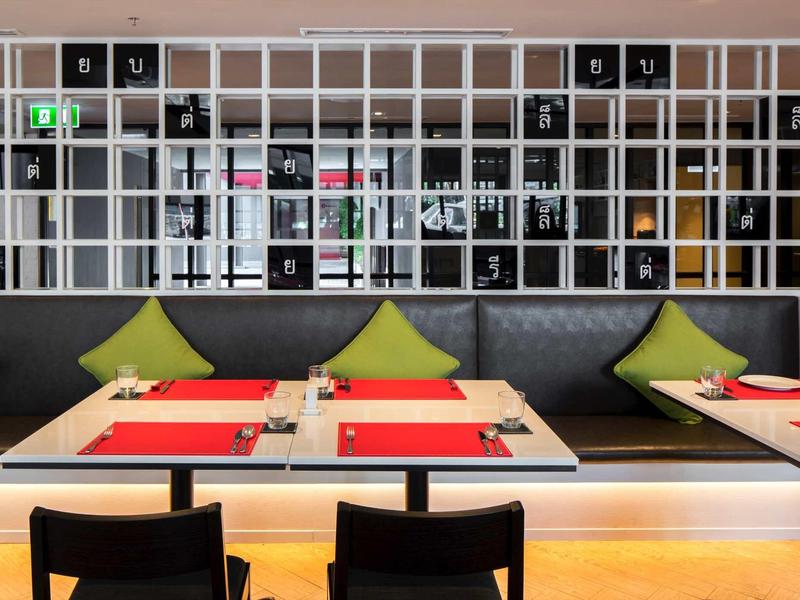 Modernes Restaurant mit grauem Polstersofa, grünen Kissen, roten Tischsets und schwarzem Stuhl.