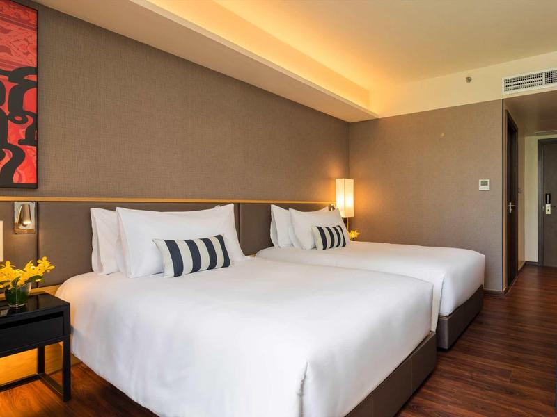 Modernes Hotelzimmer mit zwei großen Betten, weißen Bettlaken und warmem Licht.