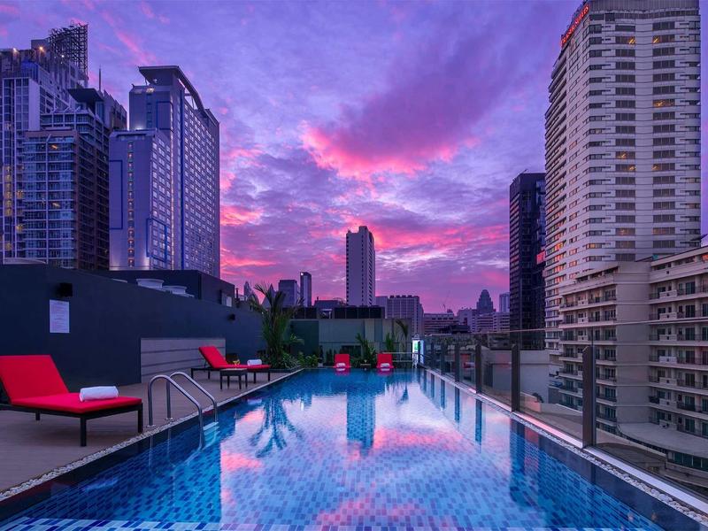 Dachpool mit Sitzbereich und Stadtblick bei Sonnenuntergang in einem Hotel.