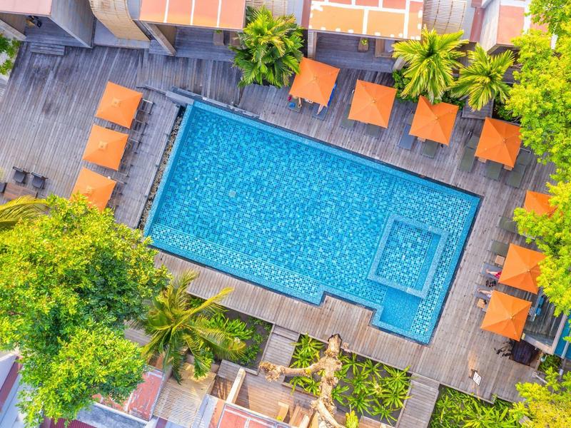 Rechteckiger Pool mit blauem Wasser, umgeben von orangen Liegestühlen und grünen Bäumen.