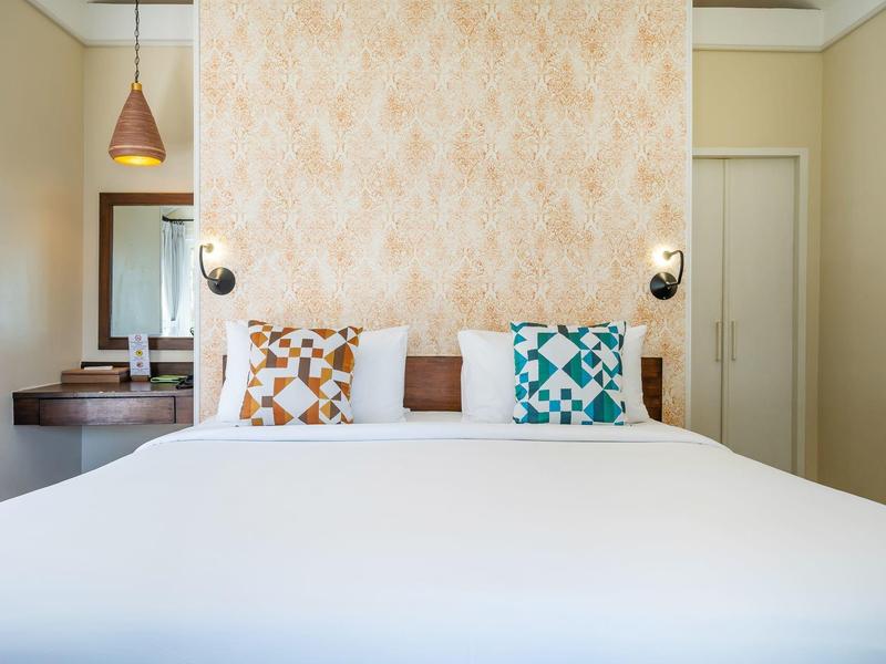 Hell eingerichtetes Schlafzimmer mit großem weißen Bett, gemusterten Kissen und nachtleuchten.