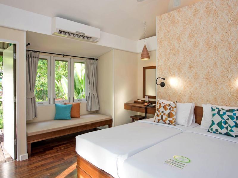 Helles Schlafzimmer mit Doppelbett, bunten Kissen, Holzboden und Sitzbank am Fenster.