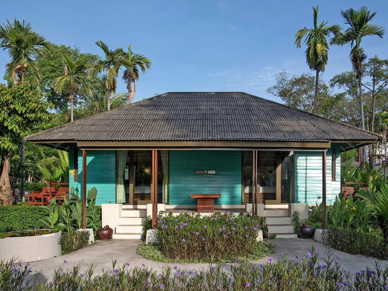 Kleines tropisches Hotelbungalow mit grün gestrichenen Wänden und umliegender Vegetation.