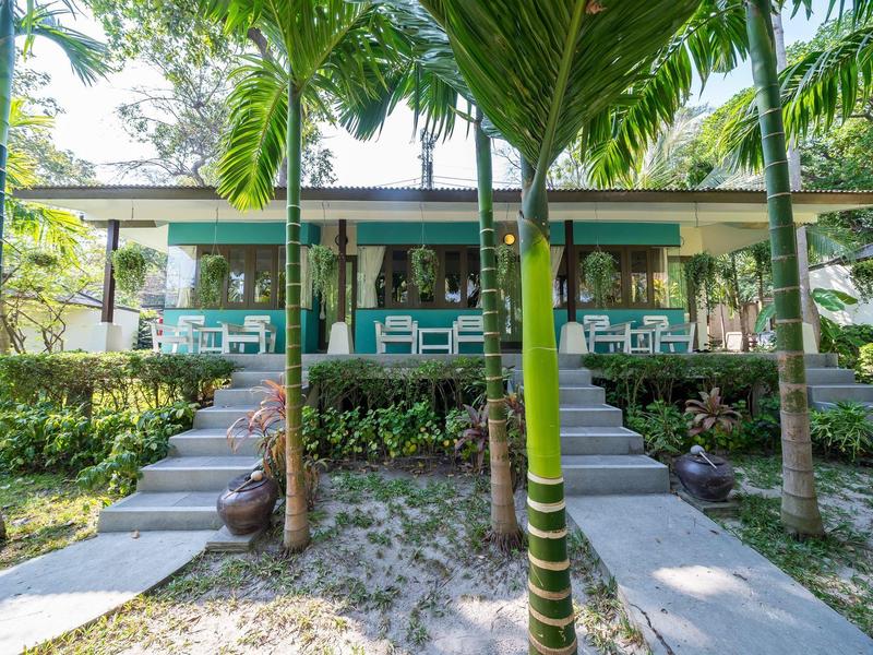 Ein Ferienbungalow mit Terrasse, umgeben von Palmen und üppiger Vegetation.