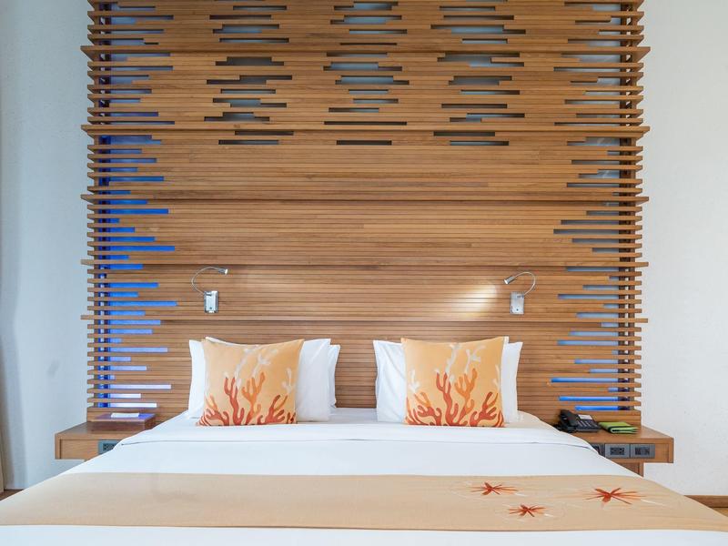 Modernes Schlafzimmer mit Holzvertäfelung, weißem Bett und Dekokissen in warmen Orangetönen.